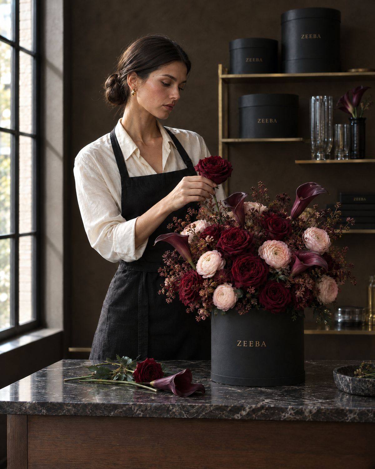 A florist in a black apron placing a burgundy rose into a black Zeeba hatbox in the Toronto atelier