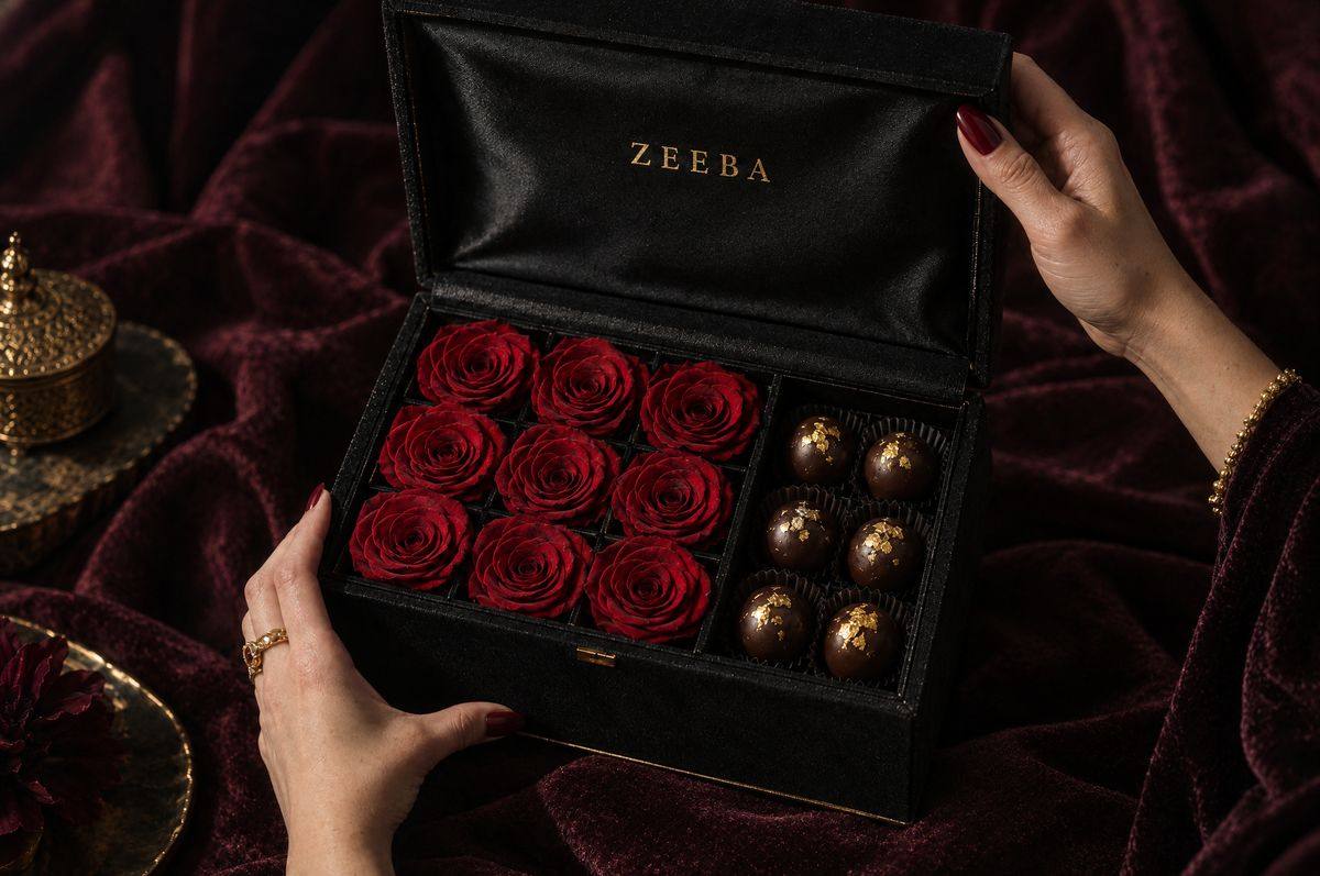 Hands opening a black Zeeba box of preserved red roses and chocolates